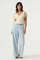 Women's cream V-neck top with crochet lace cap sleeves and a relaxed fit, styled with light wash wide-leg jeans. Front view showing the textured fabric and feminine silhouette.