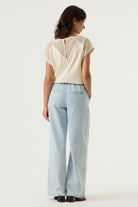 Women's cream V-neck top with crochet lace cap sleeves and back lace panel detail, shown from the back. Styled with light wash wide-leg jeans and sandals.