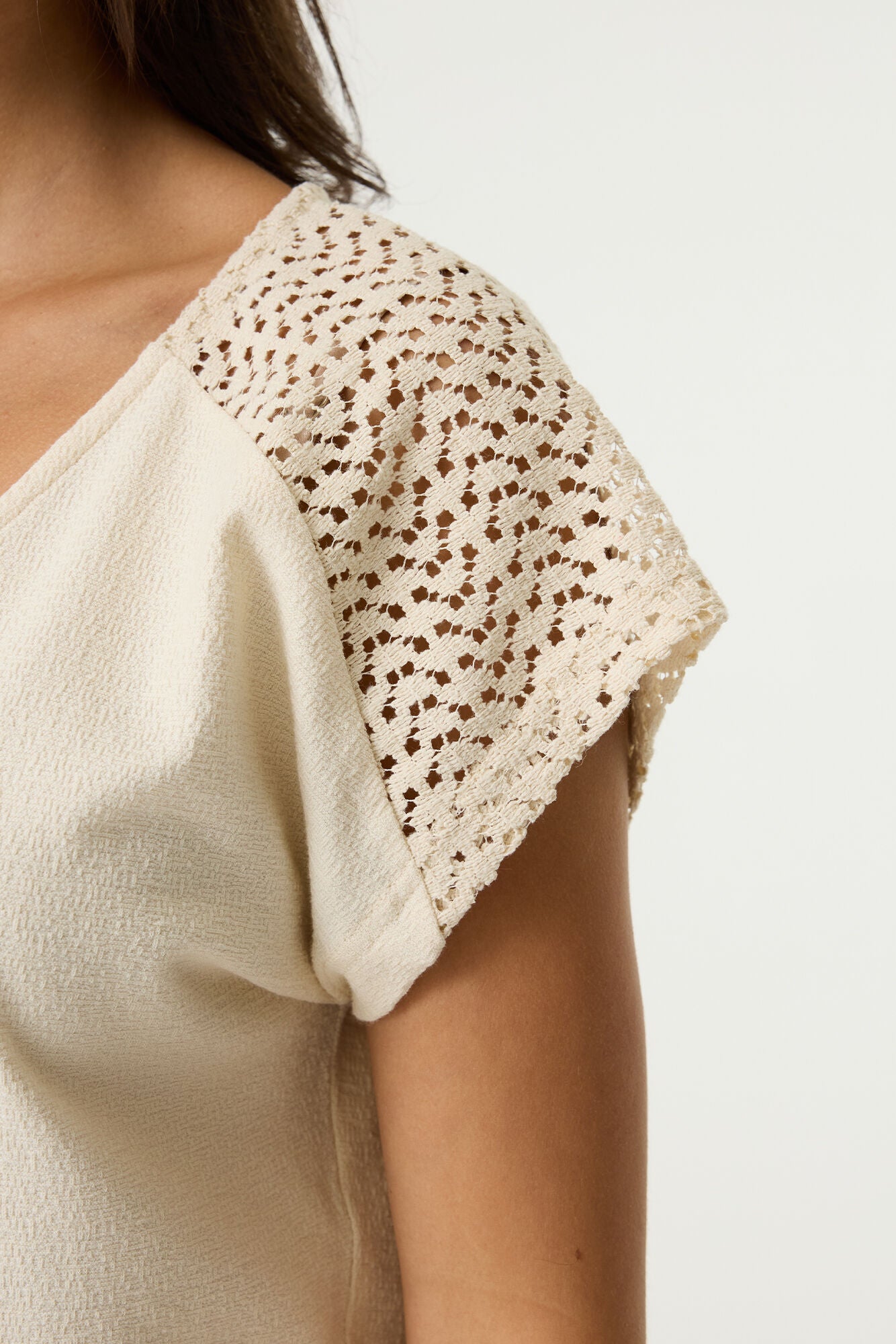 Close-up of a women's cream textured top featuring intricate crochet lace cap sleeves with an openwork pattern and delicate scalloped edging.