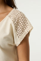 Close-up of a women's cream textured top featuring intricate crochet lace cap sleeves with an openwork pattern and delicate scalloped edging.