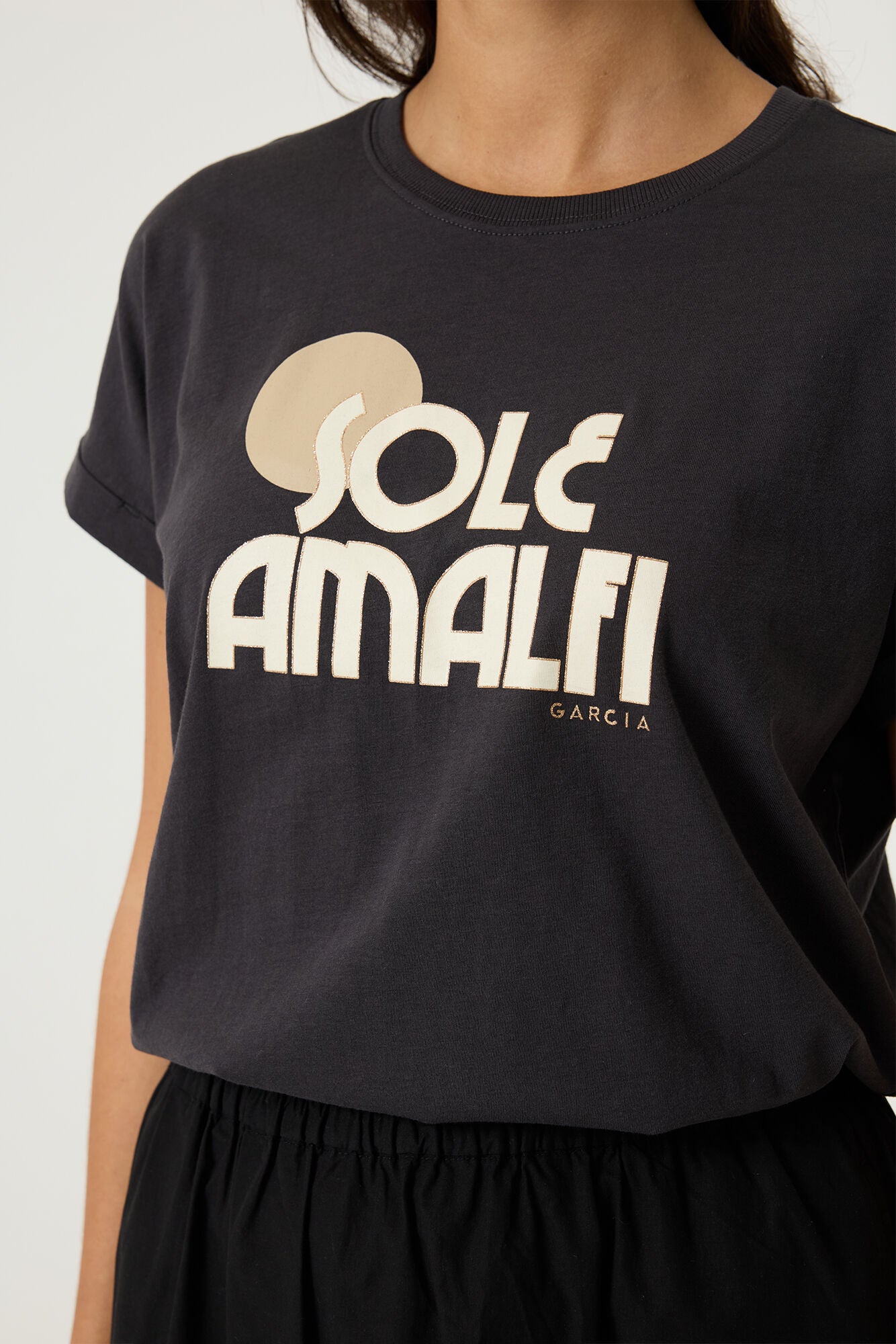 Woman wearing a charcoal relaxed fit graphic tee with “Sole Amalfi” text in light beige, styled with black pants. 