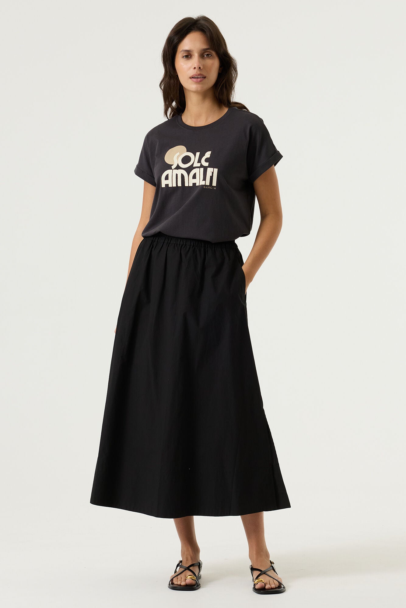 Woman wearing a charcoal relaxed fit graphic tee with “Sole Amalfi” text in light beige, styled with a black skirt.