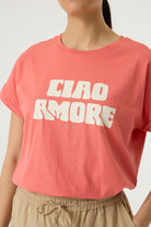 Woman wearing a coral relaxed fit graphic tee with “Ciao Amore” text in light beige, styled with beige wide-leg drawstring pants