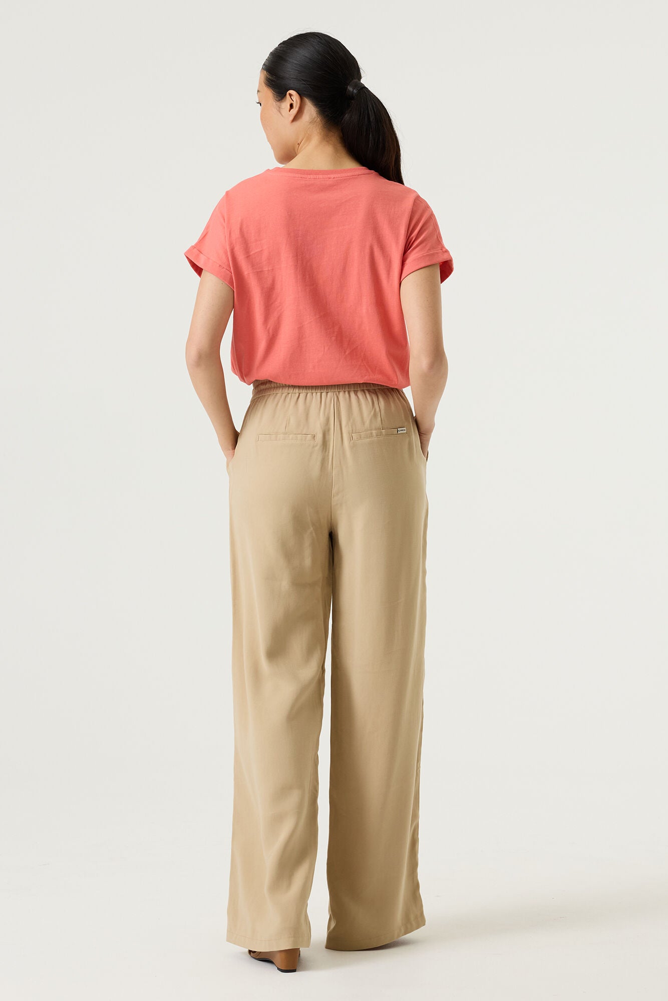 Woman wearing a coral relaxed fit graphic tee with “Ciao Amore” text in light beige, styled with beige wide-leg drawstring pants