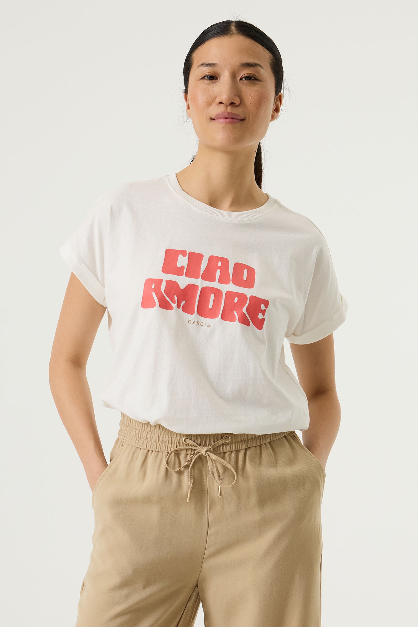 Woman wearing a white relaxed fit graphic tee with “Ciao Amore” text in pink, paired with beige wide-leg drawstring pants. 