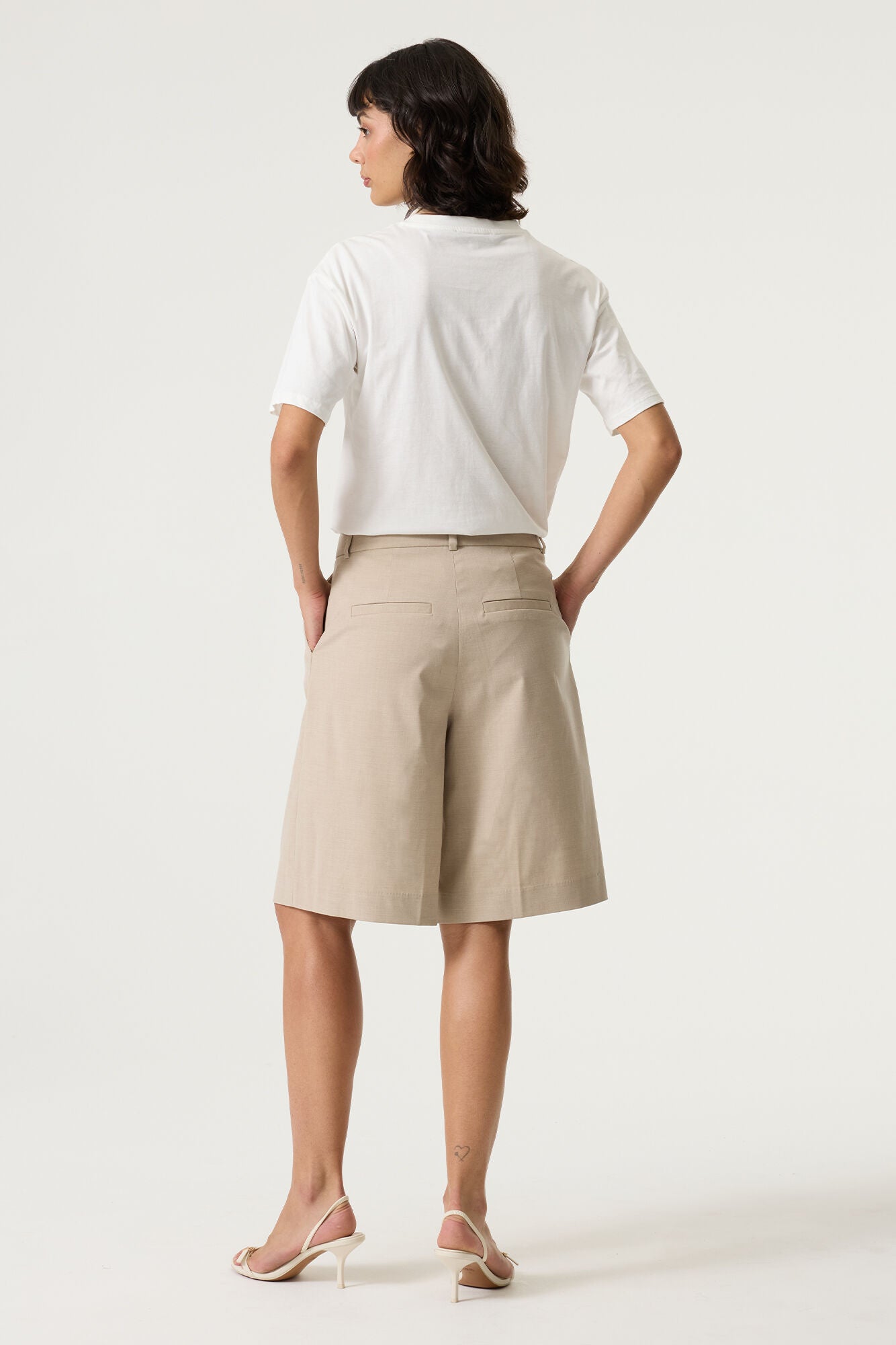 Back view of a white cotton t-shirt with a relaxed fit, paired with beige shorts and heeled sandals.