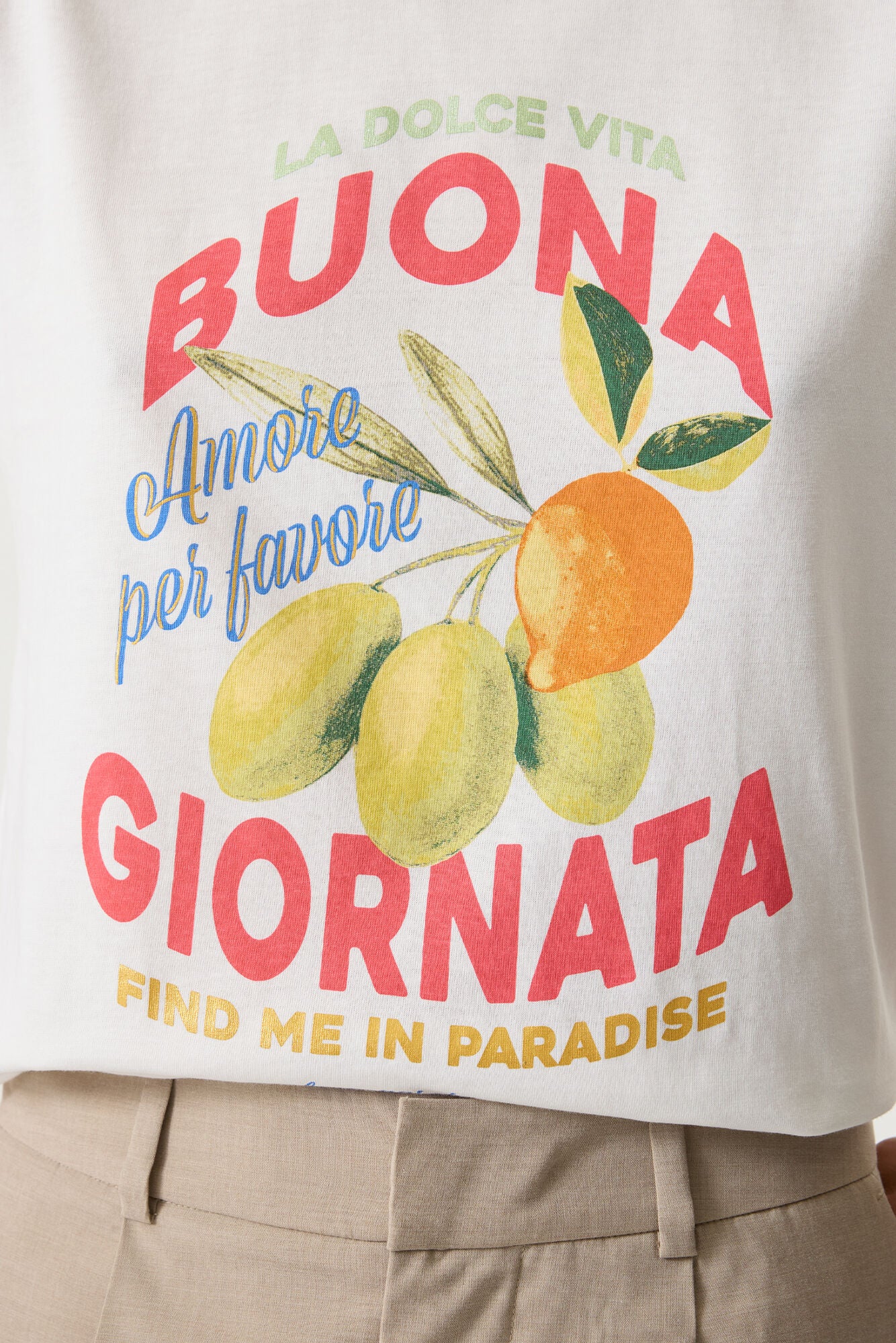 Close-up of white cotton graphic tee featuring Italian-inspired text and a lemon and olive illustration in red, blue, green, and yellow tones.