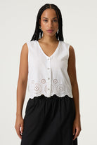 Women's white sleeveless cotton-linen blouse with eyelet embroidered scalloped hem and button-front detail. Styled with a midi skirt and shown in a relaxed front-facing pose.