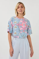 Woman wearing a floral patterned top and light gray pants on a white background