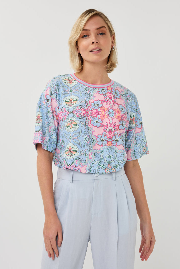 Woman wearing a floral patterned top and light gray pants on a white background