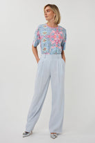 Woman wearing a floral top and light blue pants on a white background