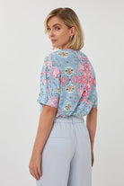 Woman wearing a floral blouse and light gray pants on a white background
