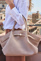 Beige handbag held by a person with a cityscape background