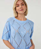 Woman wearing a light blue short-sleeve pointelle knit sweater with subtle sequin detailing, styled in a relaxed fit with a crew neckline.