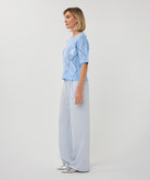 Woman wearing a light blue short-sleeve pointelle knit sweater with subtle sequin detailing, styled in a relaxed fit with a crew neckline.