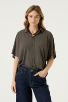 Front view of a woman wearing a brown relaxed-fit short-sleeve button-front blouse with a pointed collar, paired with dark blue jeans.