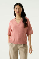 Woman modelling the Nora V-Neck Knit in pink with wide-leg beige trousers