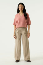 Woman modelling the Nora V-Neck Knit in pink with wide-leg beige trousers and loafers, full-length view.