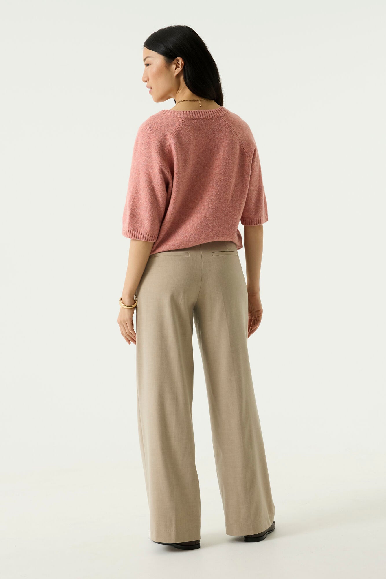 Woman modelling the Nora V-Neck Knit in pink with wide-leg beige trousers
