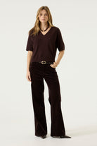 Woman modelling the Nora V-Neck Knit in dark brown with wide-leg dark trousers, belt, and pointed-toe shoes, full-length view.