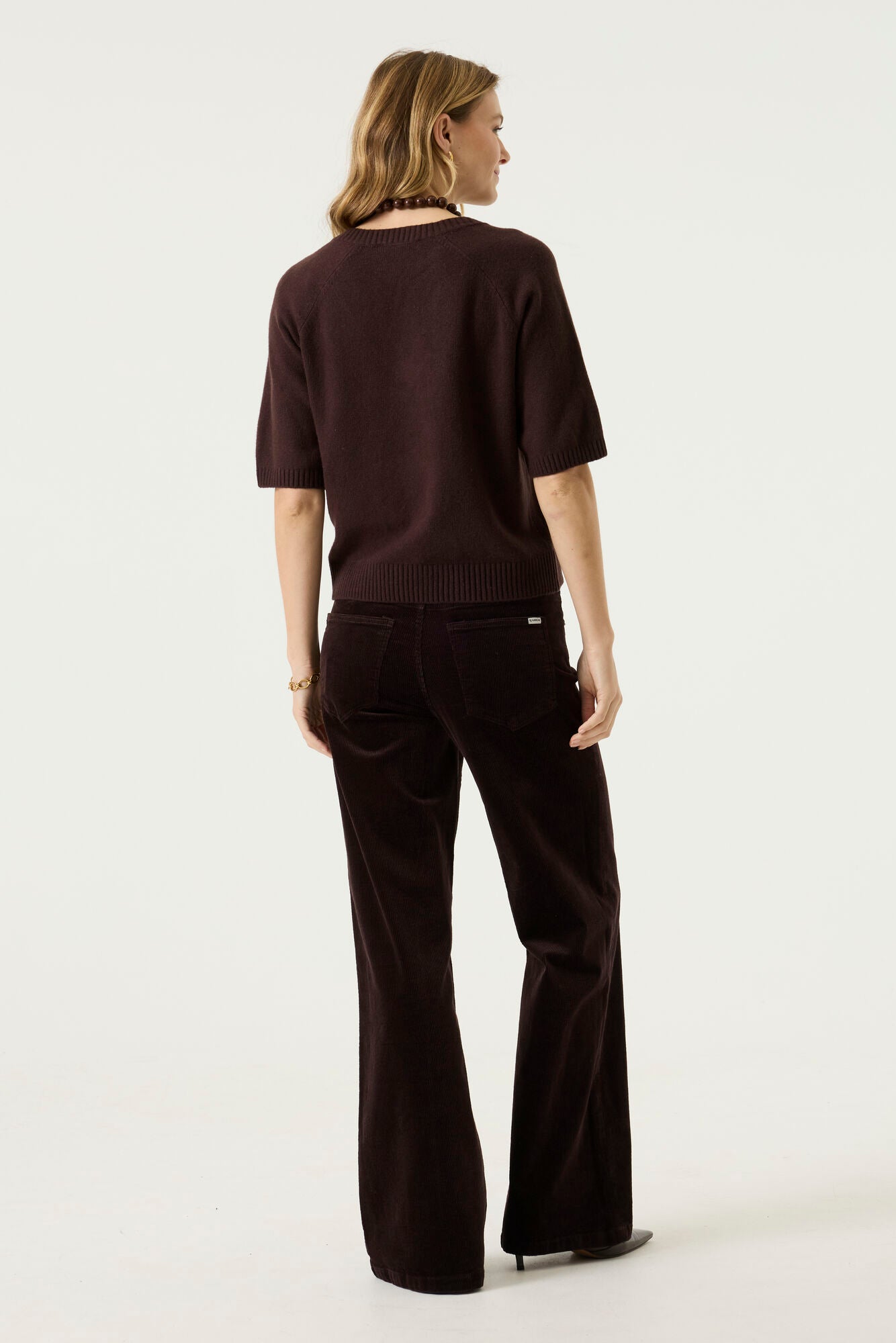 Woman modelling the Nora V-Neck Knit in dark brown with wide-leg dark trousers