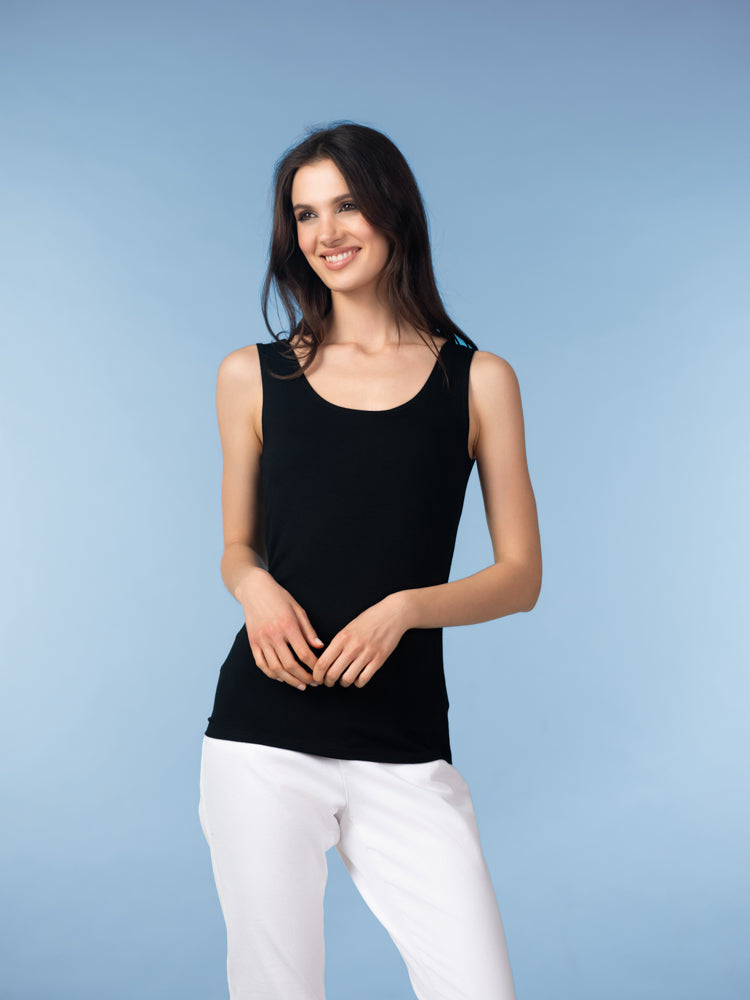 Front view of model smiling in a black scoop neck tank top paired with white pants against a soft blue studio backdrop.
