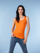 Woman wearing an orange sleeveless tank top with denim jeans.