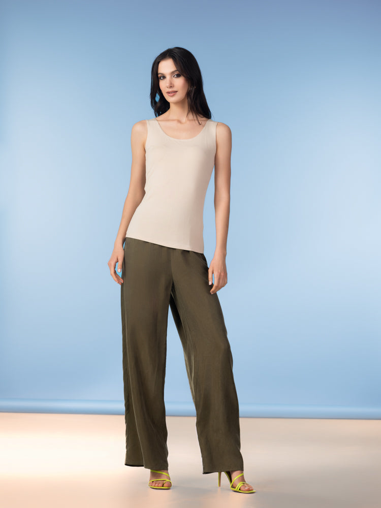 Woman wearing a beige sleeveless tank top with olive wide-leg trousers and lime green heeled sandals against a blue background.