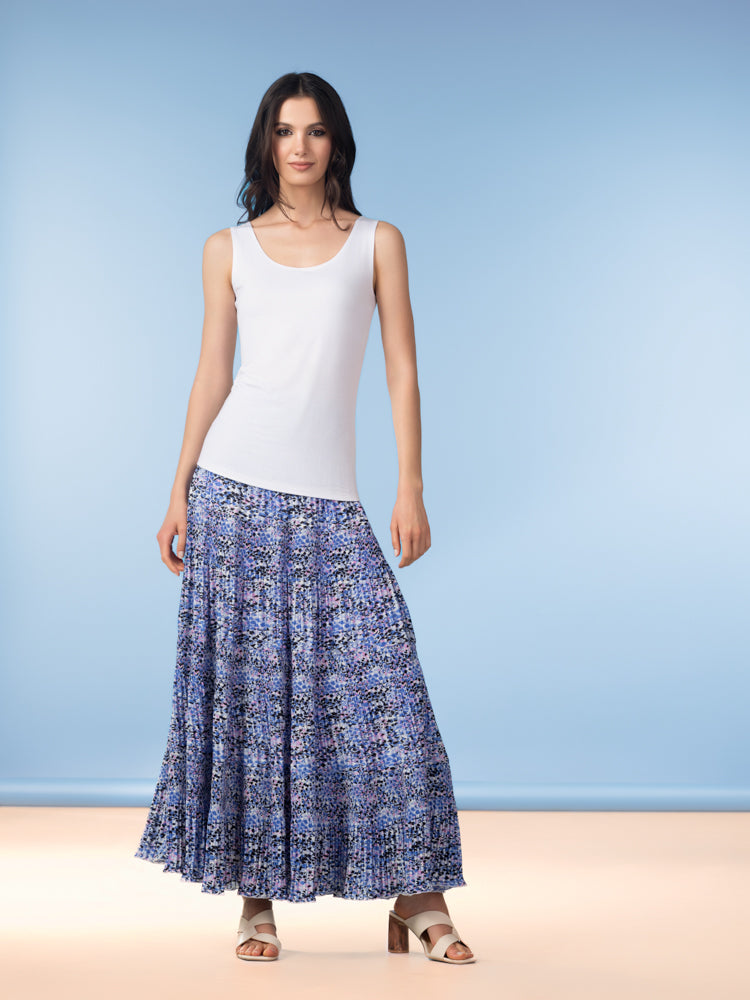 Woman wearing a white sleeveless tank top with a blue floral maxi skirt and beige heeled sandals against a blue background.