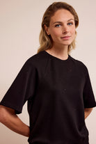 Woman wearing a black t-shirt with small rhinestones against a beige background