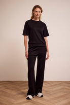 Person wearing a black outfit standing on a wooden floor with a beige wall background