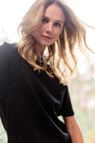 Woman wearing a black top with small embellishments against a blurred natural background