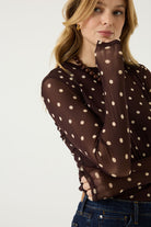 Woman wearing a brown long-sleeve mesh top with cream polka dots, dark blue jeans