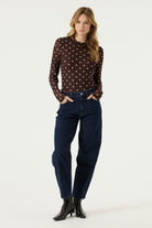 Woman wearing a brown long-sleeve mesh top with cream polka dots, dark blue jeans, and black heeled ankle boots.