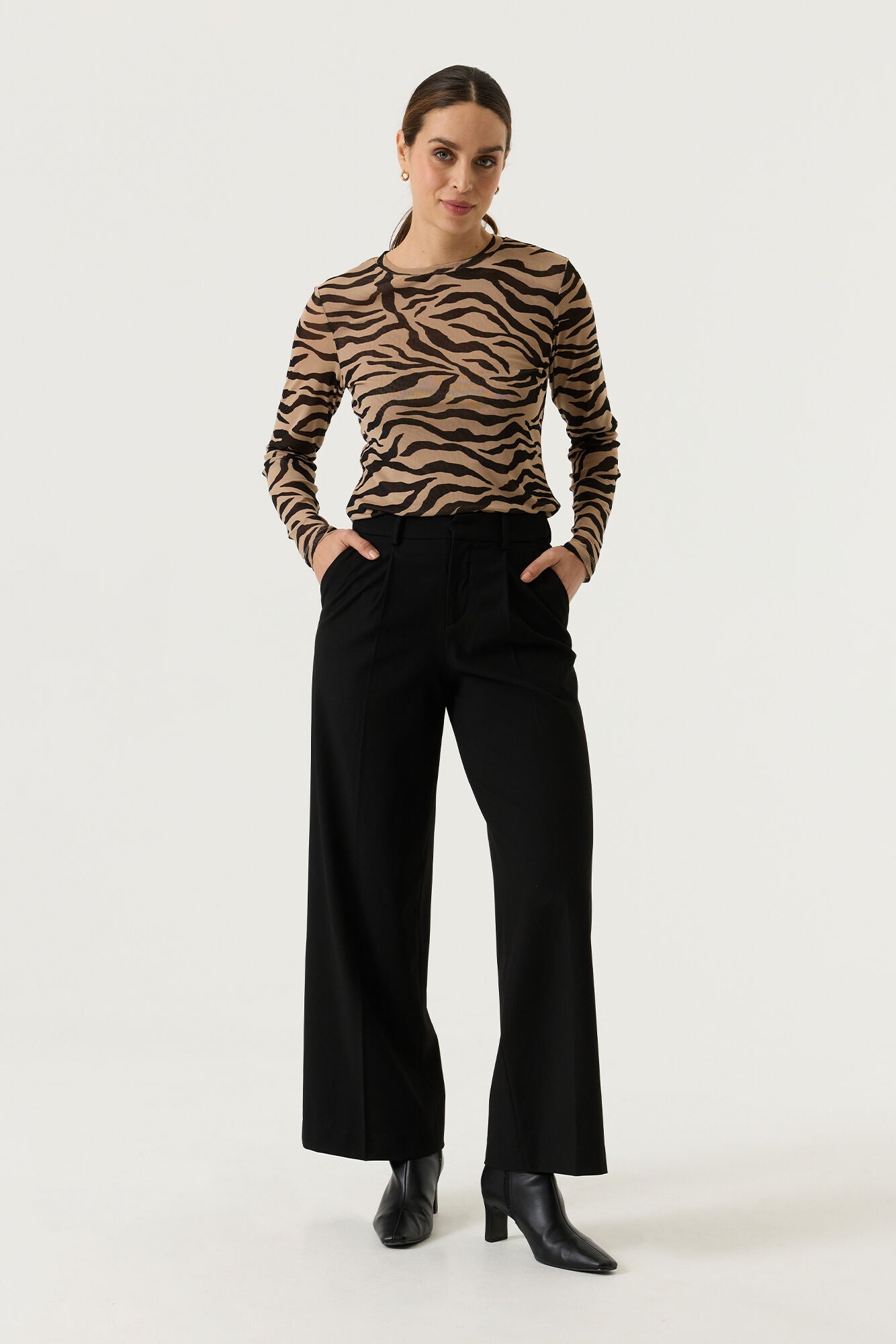 Woman wearing a tan and black zebra-print long-sleeve top with black wide-leg trousers and black heeled ankle boots.