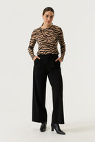 Woman wearing a tan and black zebra-print long-sleeve top with black wide-leg trousers and black heeled ankle boots.