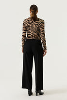 Back view of a woman wearing a tan and black zebra-print long-sleeve top with black wide-leg trousers and black heeled ankle boots.