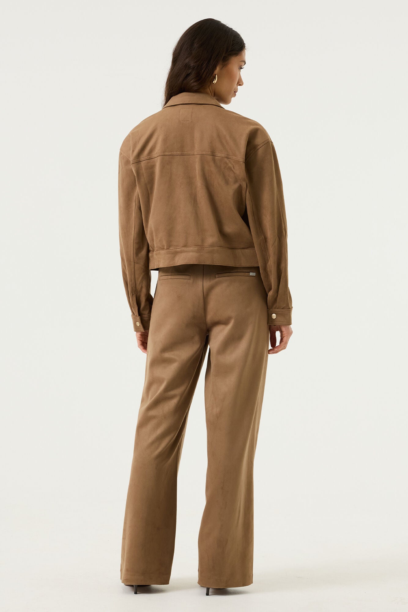 Back view of a woman wearing the Aspen cropped utility jacket in brown, featuring a cropped hem, long sleeves and structured seaming.