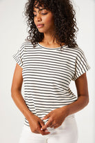 Women's black and white striped knit t-shirt featuring a relaxed silhouette, rolled short sleeves, and round neckline. Paired with grey slim-leg jeans and chunky sneakers.