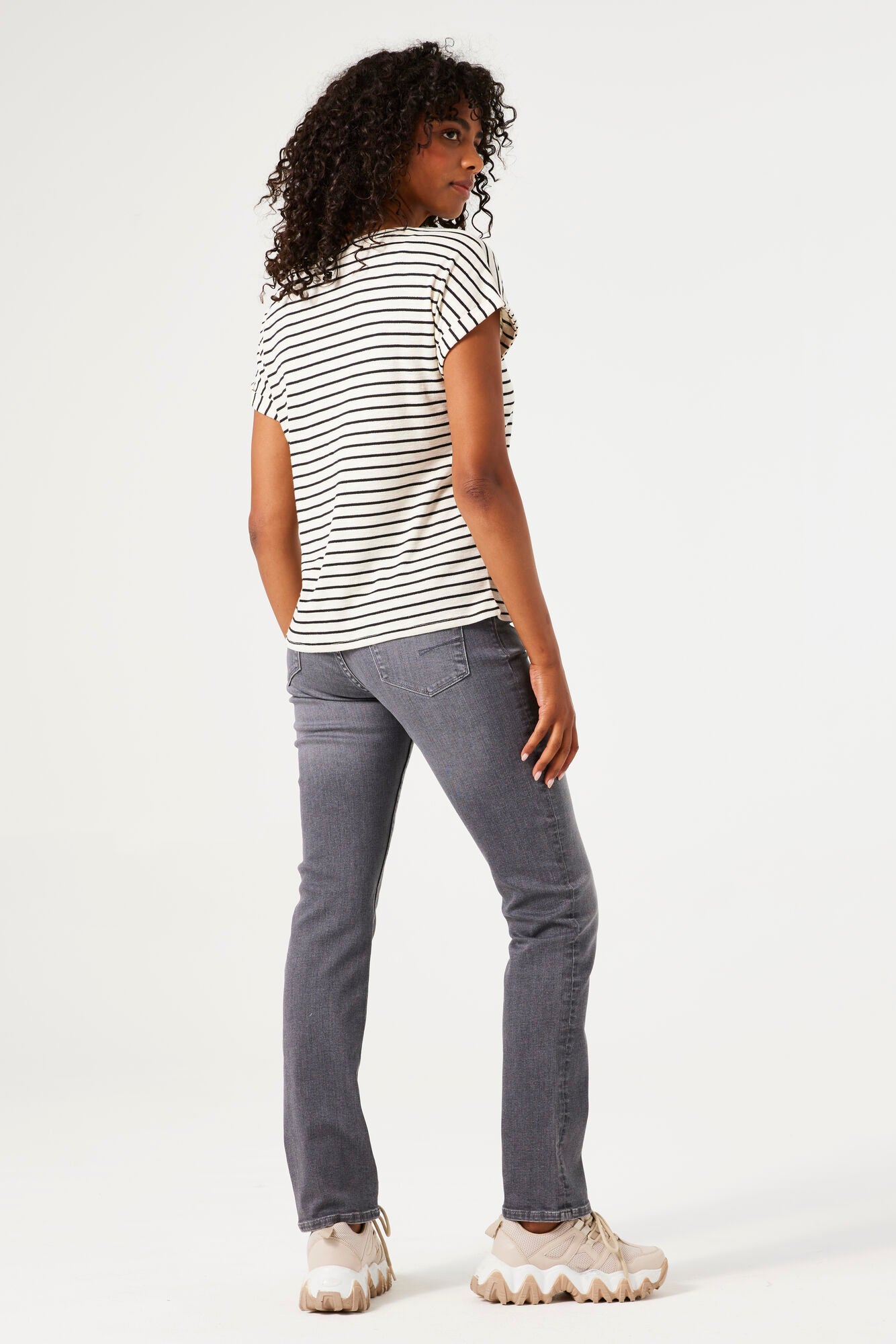 Women's black and white striped knit t-shirt with a relaxed fit, rolled short sleeves, and round neckline, shown from the back. Styled with grey slim-leg jeans and chunky sneakers.