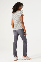 Women's black and white striped knit t-shirt with a relaxed fit, rolled short sleeves, and round neckline, shown from the back. Styled with grey slim-leg jeans and chunky sneakers.