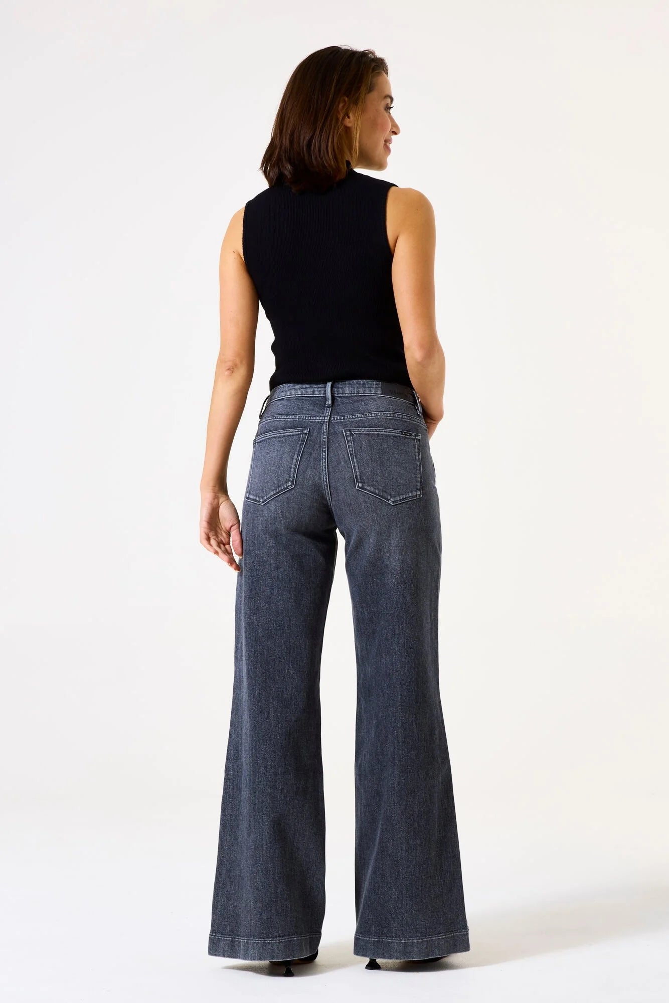 Women's ribbed mock neck sleeveless knit top shown from the back, featuring a fitted silhouette and clean finish. Styled with wide-leg denim jeans to showcase the top's versatile everyday appeal.