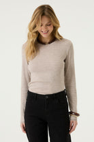 Woman wearing a beige ribbed long-sleeve tee with a crew neckline and fitted silhouette, paired with black jeans.