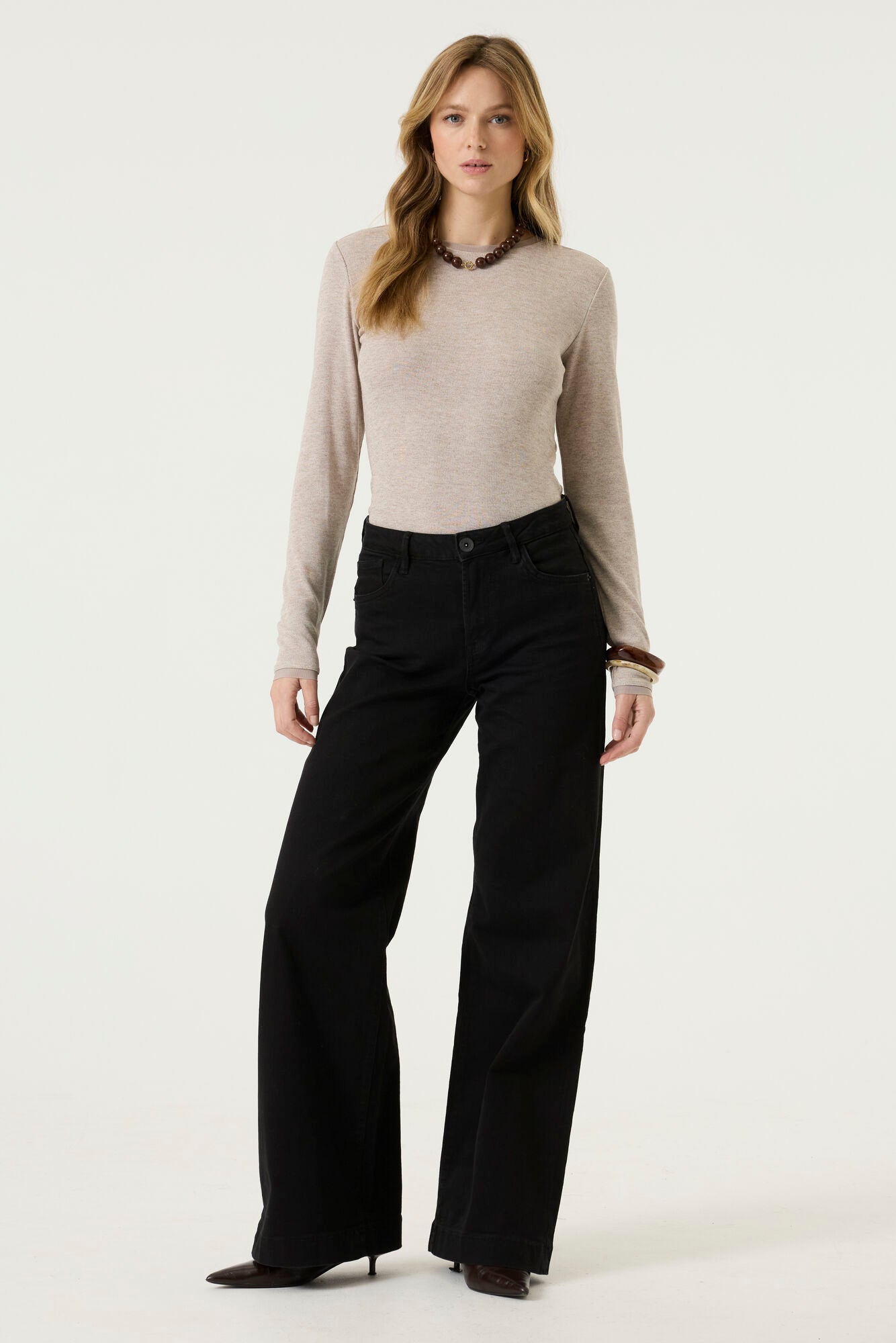 Woman wearing a beige ribbed long-sleeve tee with a crew neckline and fitted silhouette, paired with black jeans.