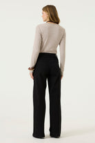 Back view of a woman wearing a beige ribbed long-sleeve tee with a fitted silhouette and full-length sleeves.