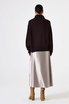 Person wearing a dark sweater and light-colored skirt on a white background