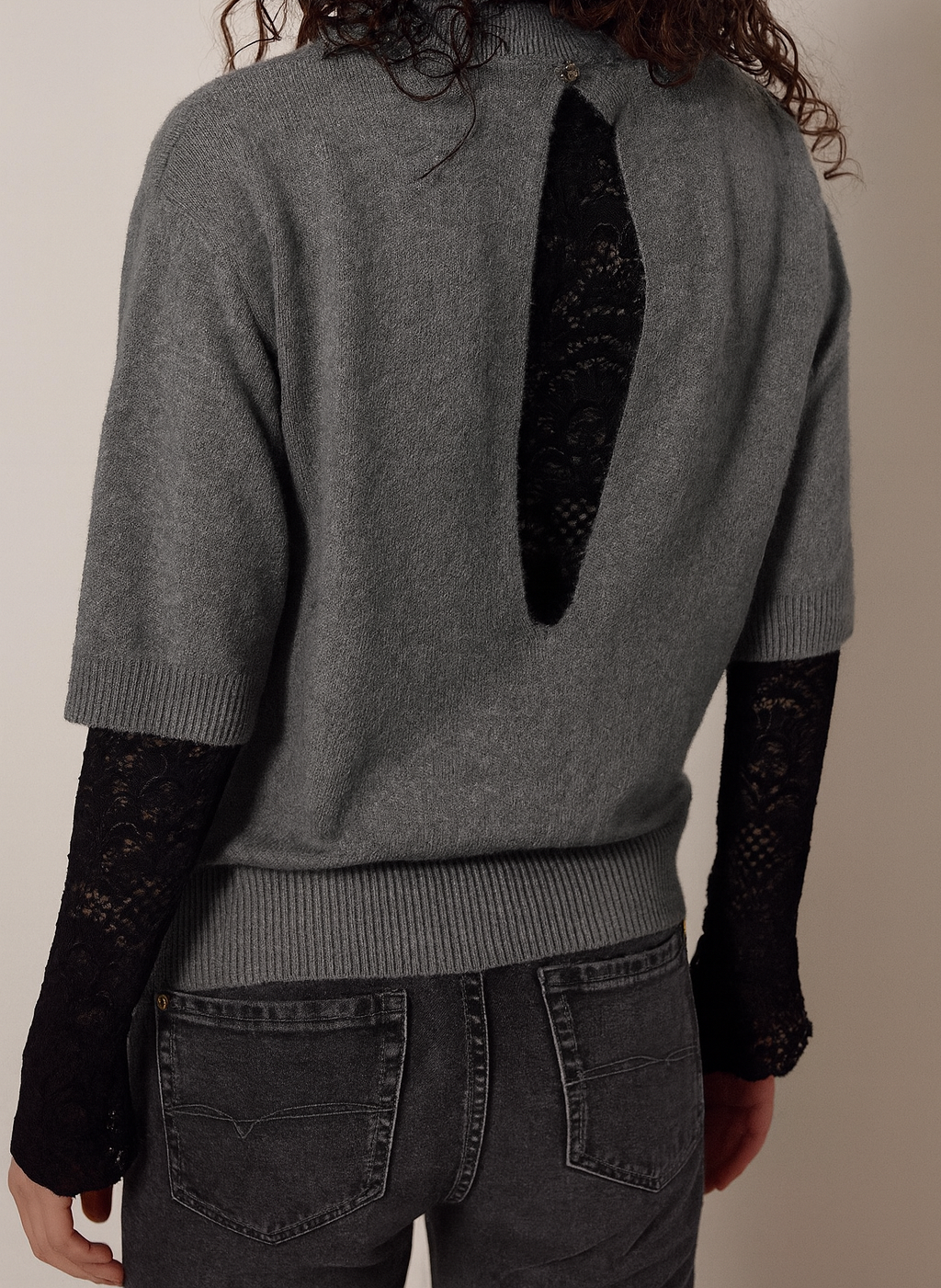 Person wearing a gray sweater with a unique cutout design on the back, paired with black sleeves and pants.