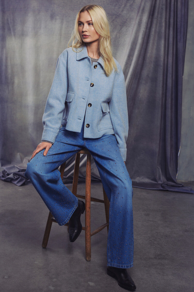Model wearing a wool-blend cropped jacket with oversized buttons and flap pockets, styled with denim pants.