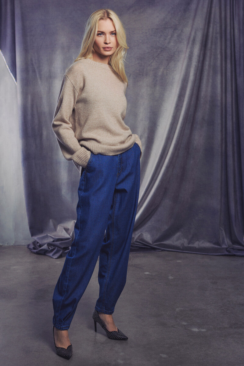Model in sweater and tapered barrel-leg jeans on a gray backdrop, showcasing a modern casual style.