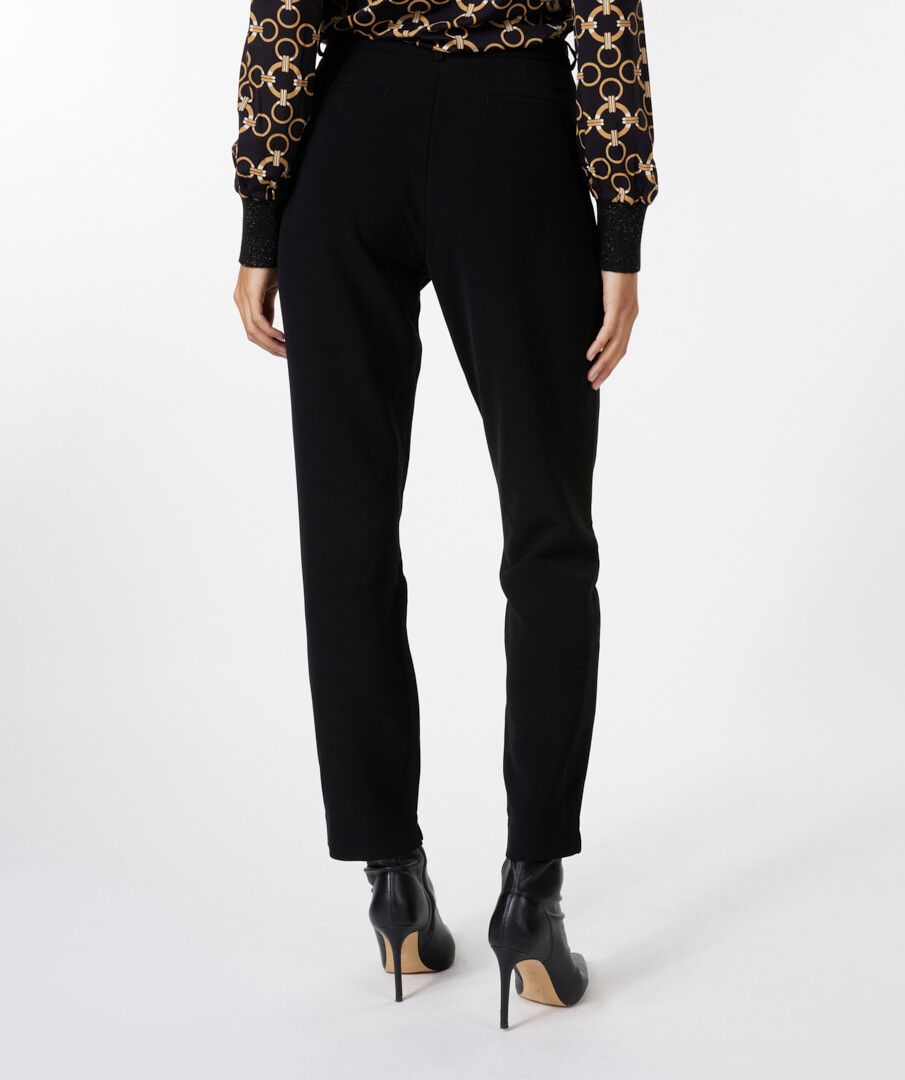 Person wearing a patterned blouse and black pants on a white background